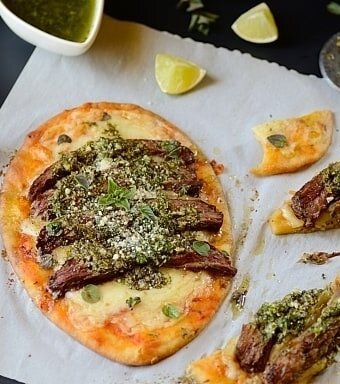 one meat flatbread on a table with some flatbread slices and garnishes on the sides