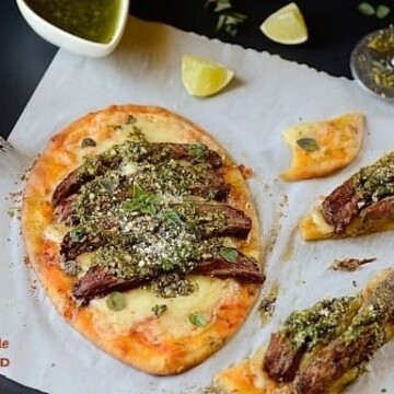 one meat flatbread on a table with some flatbread slices and garnishes on the sides