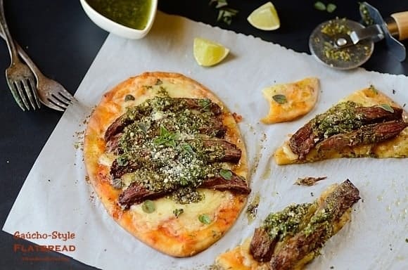 one meat flatbread on a table with some flatbread slices and garnishes on the sides