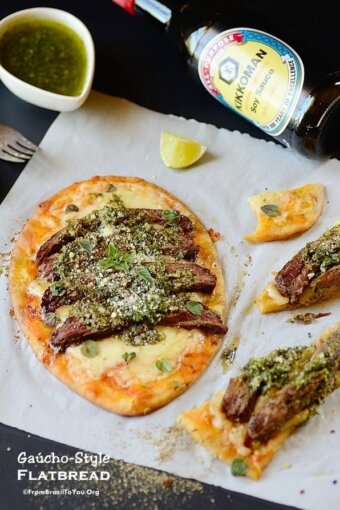 one meat flatbread on a table with some flatbread slices and garnishes on the sides