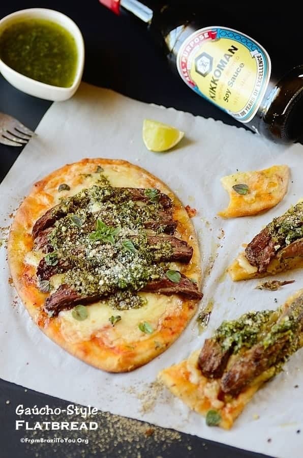 one meat flatbread on a table with some flatbread slices and garnishes on the sides