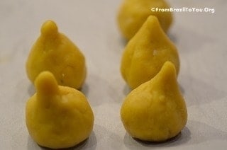 The drumstick-shaped chicken fritters are resting on a sheet of parchment paper before dredging in flour