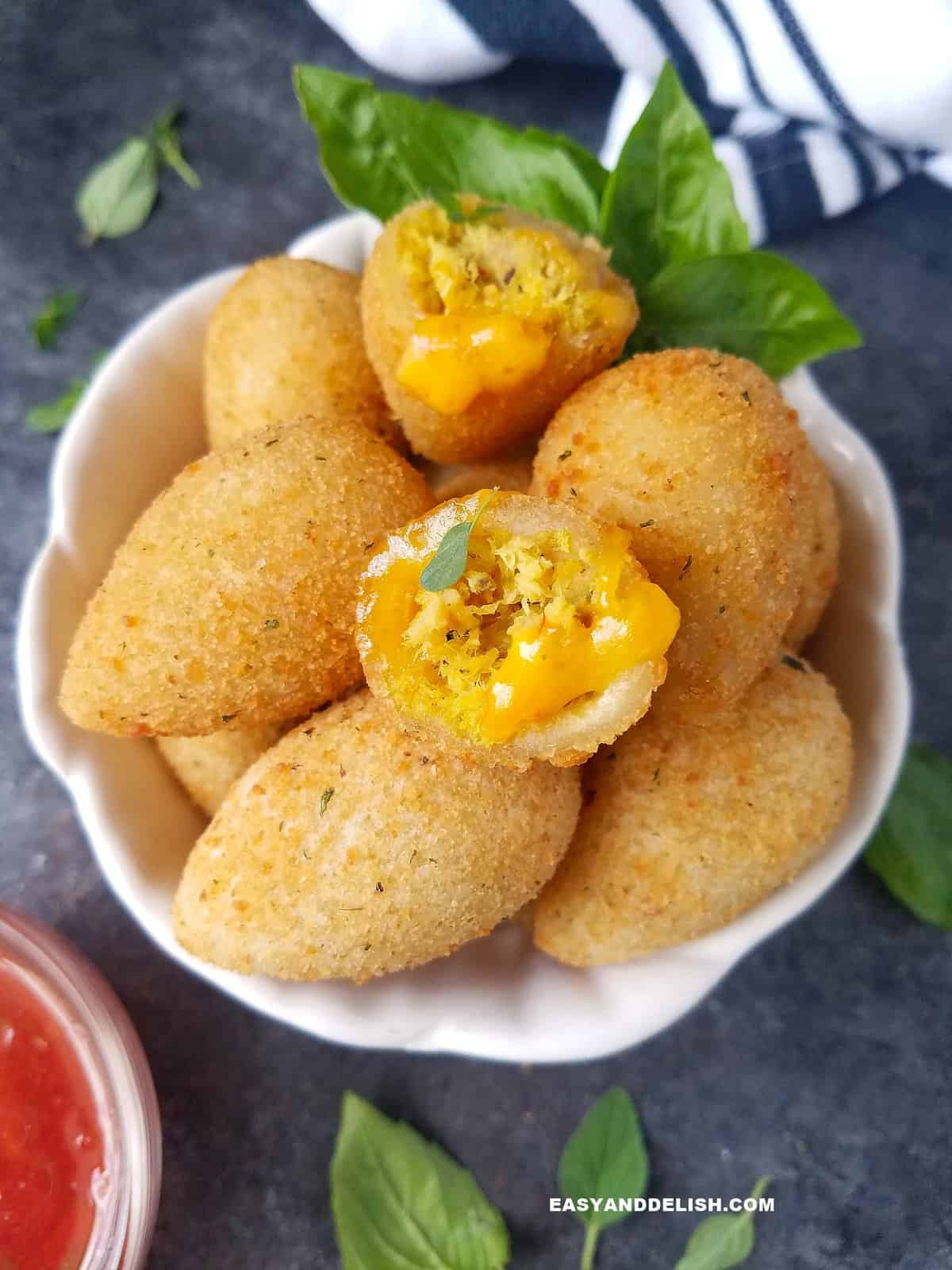 A serving bowl filled with chicken croquettes for a party with some fresh herbs on the side.