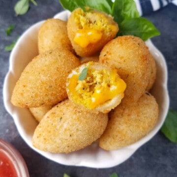 A serving bowl filled with chicken croquettes for a party with some fresh herbs on the side.