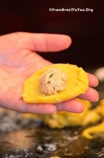 A disc of coxinha dough held in the palm of the hand, with chicken filling in the center