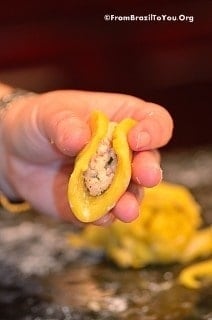 A hand holds a disc of coxinha dough folded lengthwise around the chicken filling
