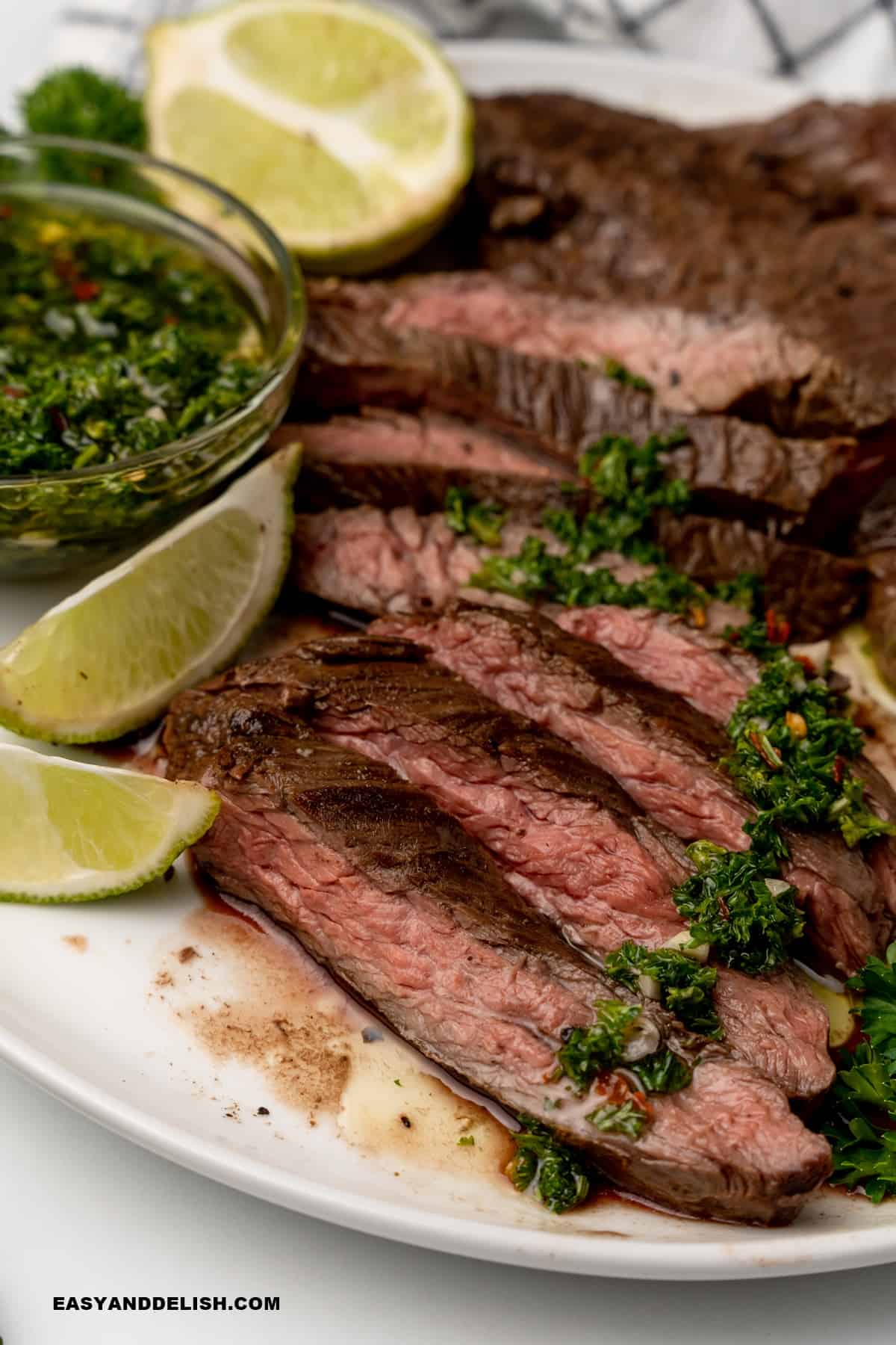 sliced skirt steak topped with chimichurri sauce with lime wedges on the side