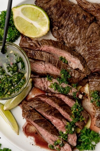 skirt steak with chimichurri sauce and lime wedges in a plate.