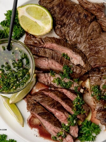 skirt steak with chimichurri sauce and lime wedges in a plate.