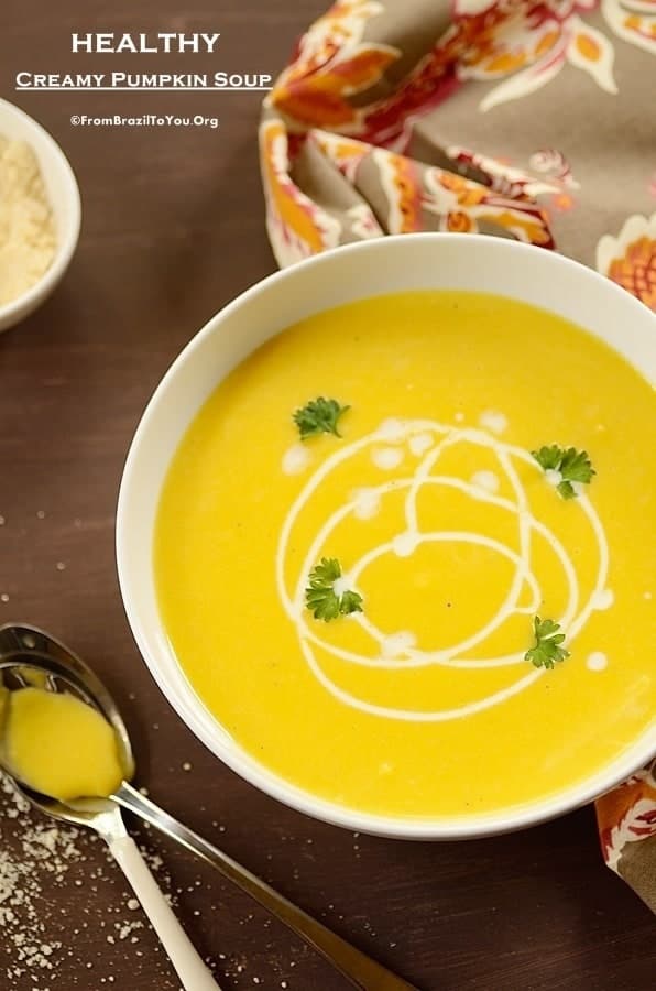 a bowl of creamy pumpkin soup drizzled with heavy cream and spoons on the side