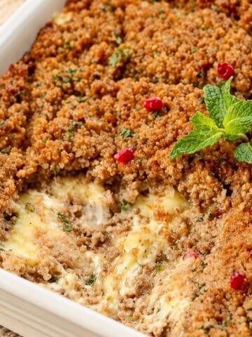 Baked kibbeh with a golden crust, melted cheese filling, fresh mint, and pomegranate seeds.