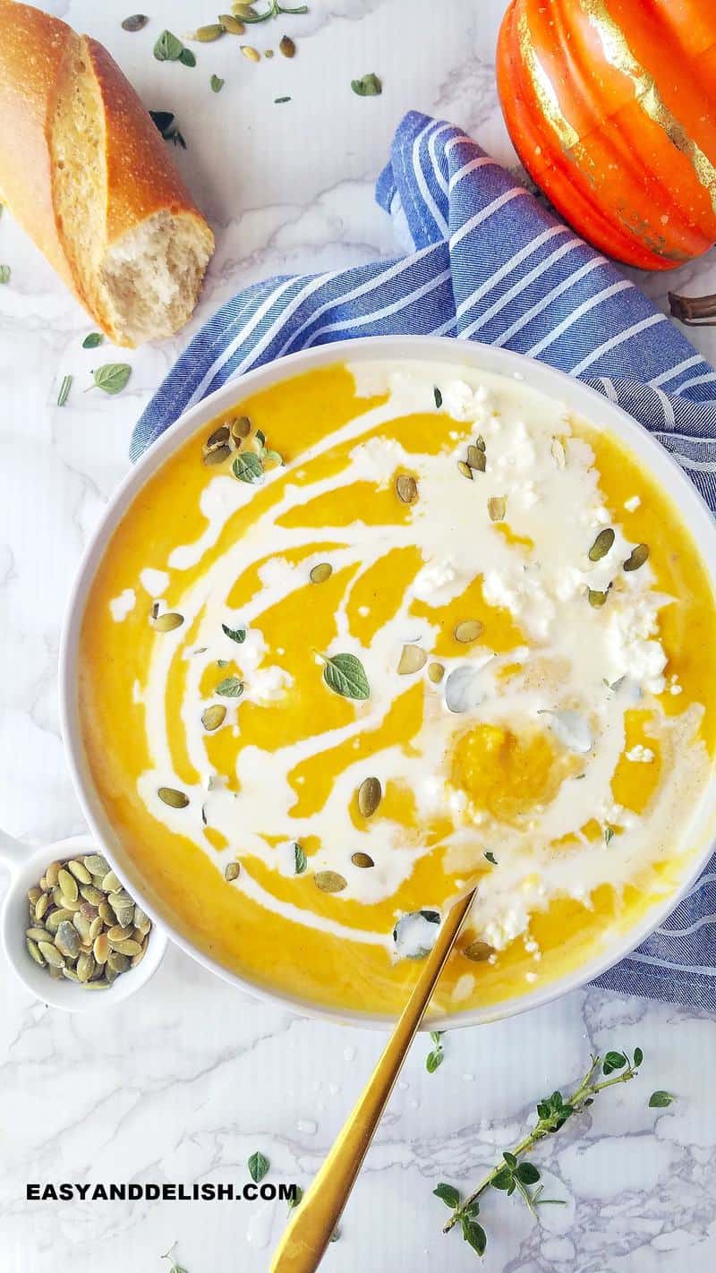 a bowl of pumpkin soup with garnishes on the side and bread
