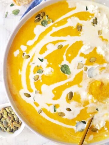 close up of a bowl of vegan pumpkin soup drizzled with coconut milk
