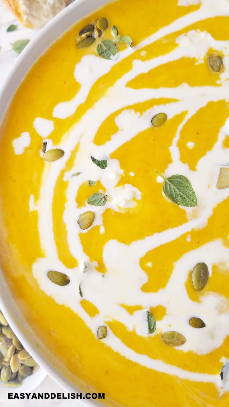 close up image of creamy pumpkin soup topped with herbs and pepitas