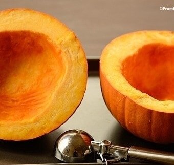 Two sliced pumpkin halves with their centers scooped clean with an ice cream scoop