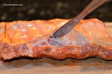 A dull butter knife is slipped beneath the membrane of the baby back ribs