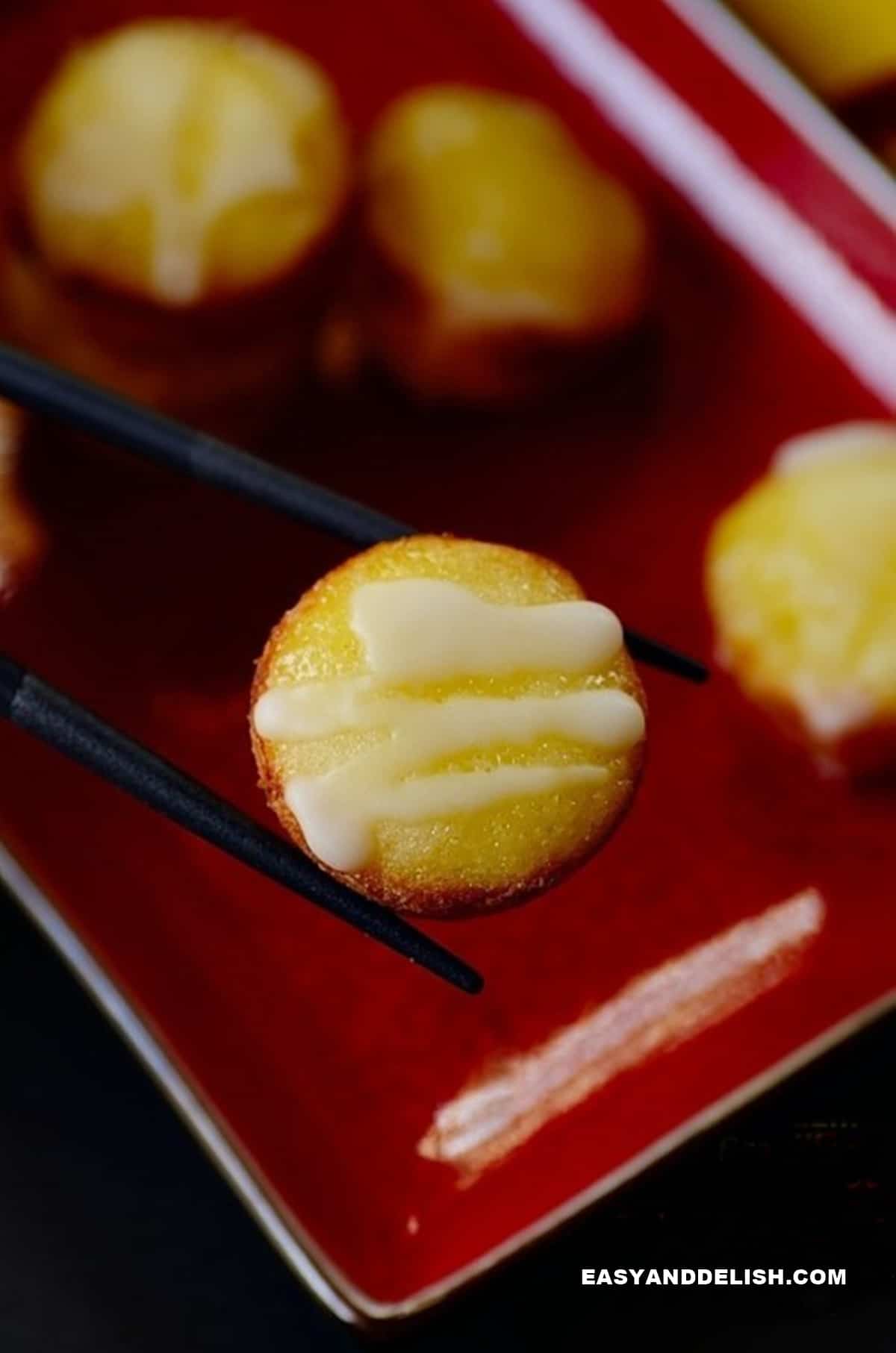 a tray with sweet rice cakes and one held between chopsticks.