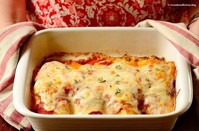 cook holding a bakish dish with chicken parmigiana inside