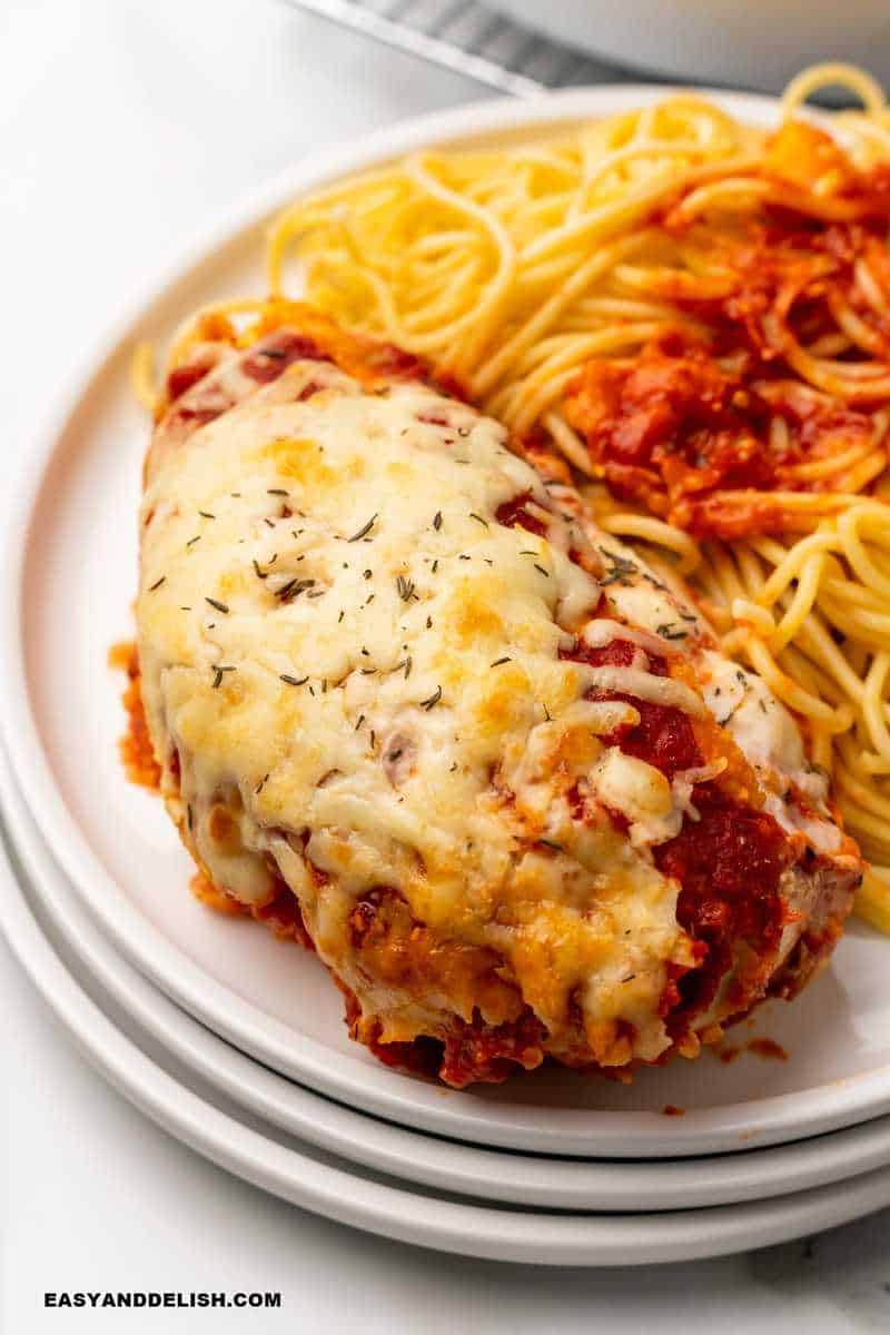 a plate with spaghetti and a breast of chicken parmesan