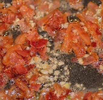 Pieces of chopped sauteed garlic and bacon simmering together in a pan