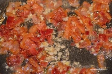 Pieces of chopped sauteed garlic and bacon simmering together in a pan