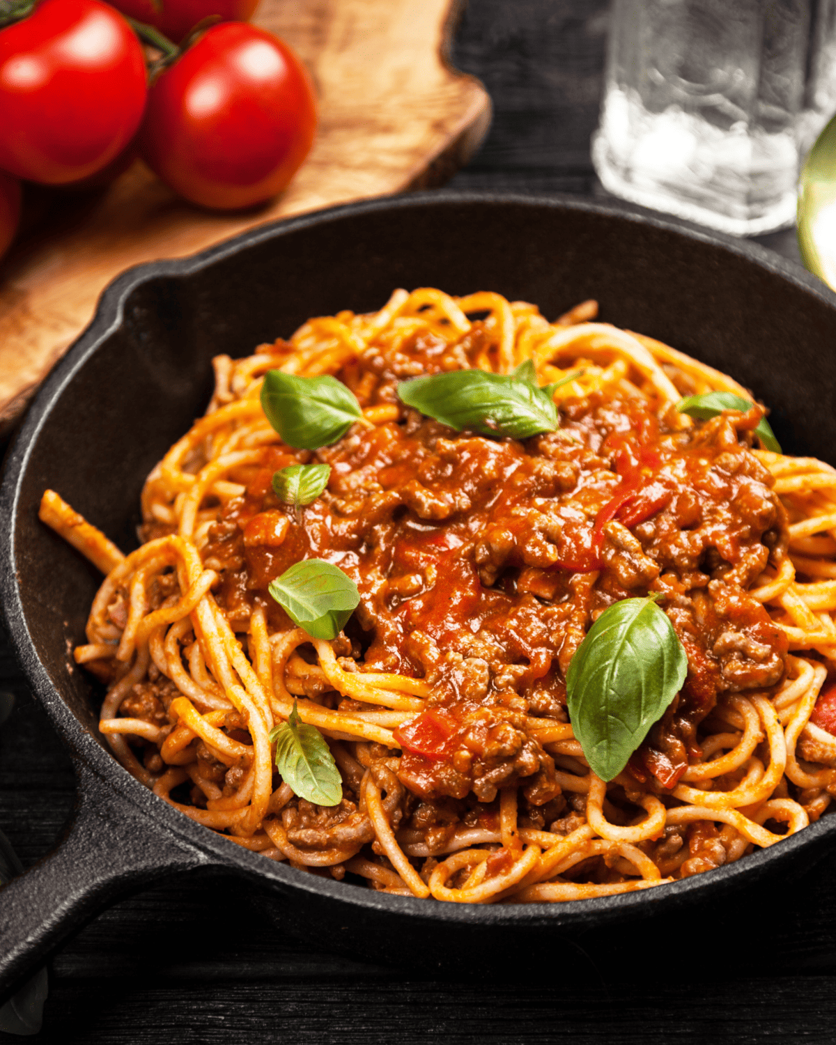 close up of a skillet with spaghetti and meat sauce garnished with fresh basil leaves.