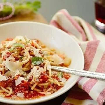 Pasta with meat sauce and shave cheese in a white dish and a spoon