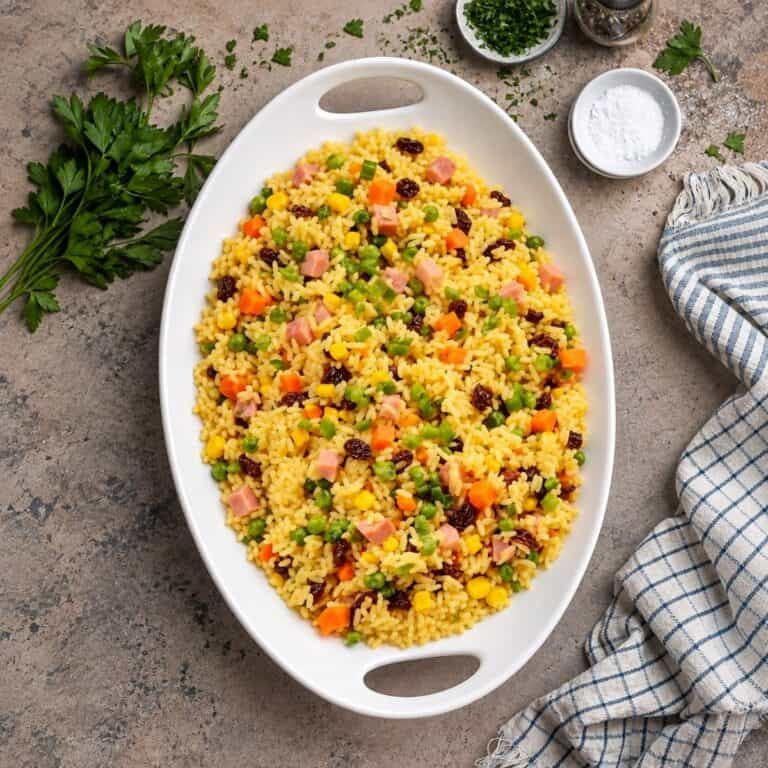 Overhead view of colorful Brazilian rice with ham, vegetables, and raisins.