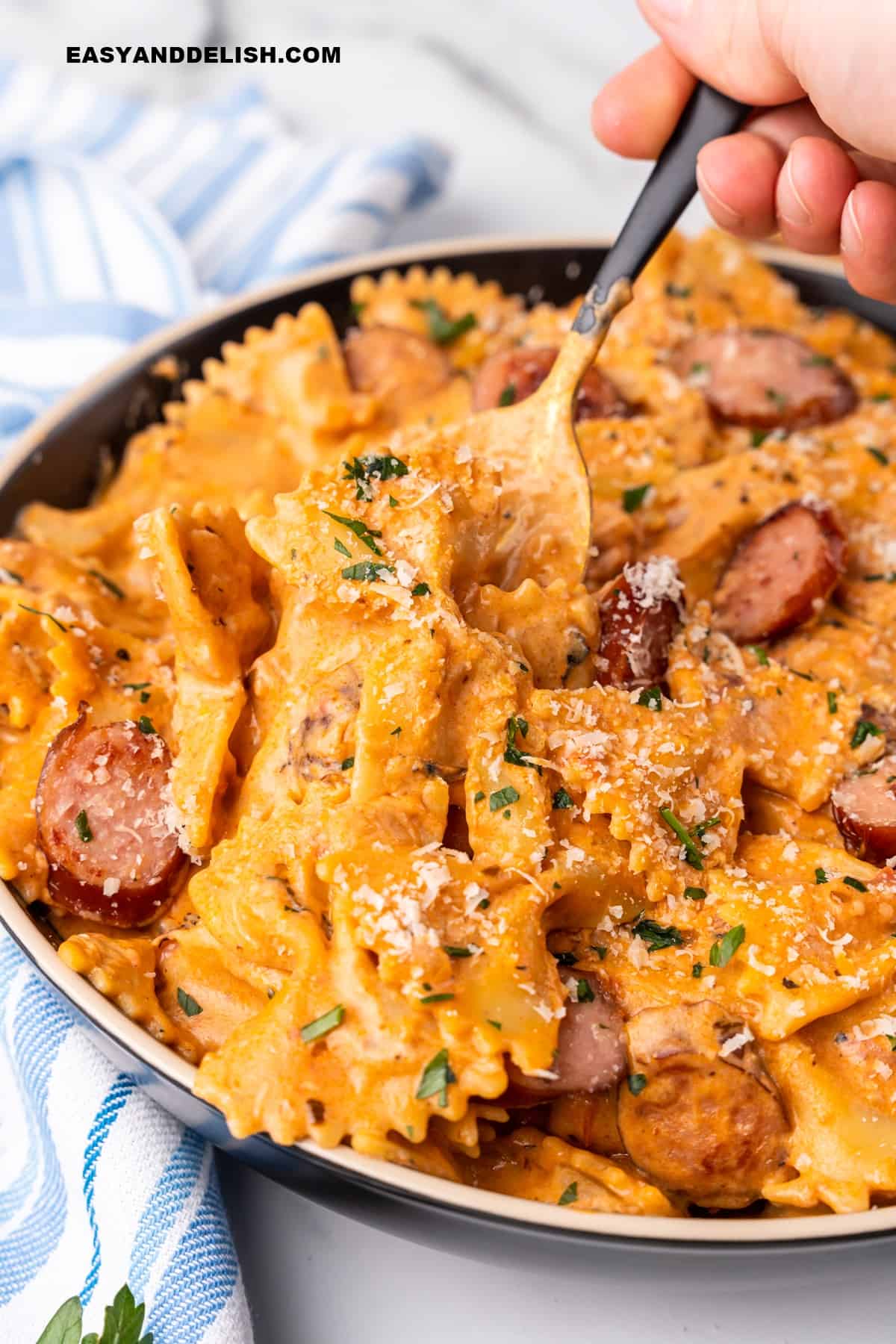 A plate with pasta with sausage and a spoon picking up part of the pasta.