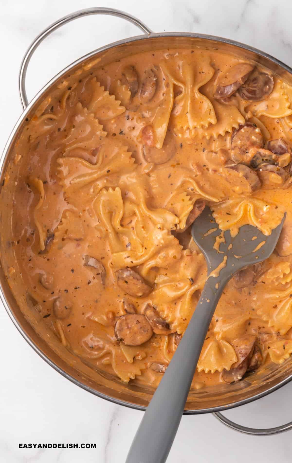 Creamy sausage pasta in a pan with a serving spoon in the middle.