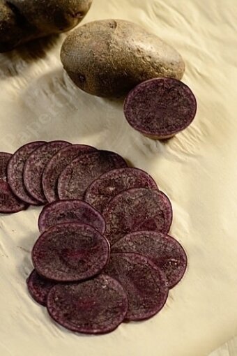 Many round slices of purple potatoes on a sheet of wax paper