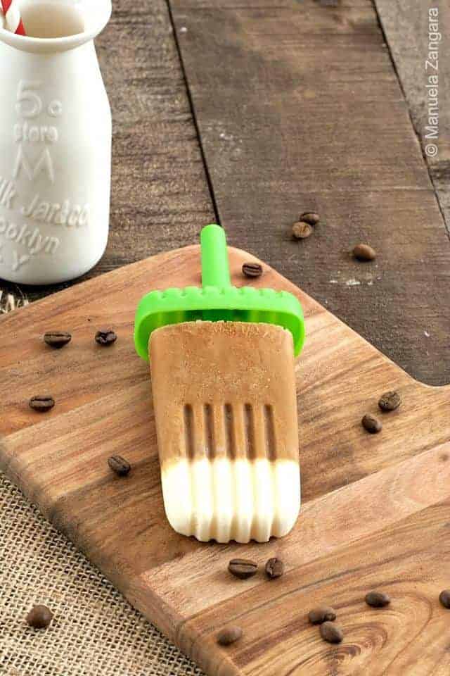 Coffee cream popsicle on a wood cutting baord with coffee beans