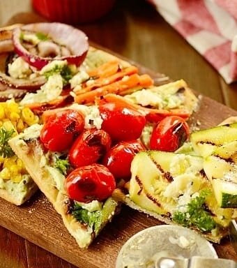 grilled vegetable pizza on a wooden board with a pizza cutter