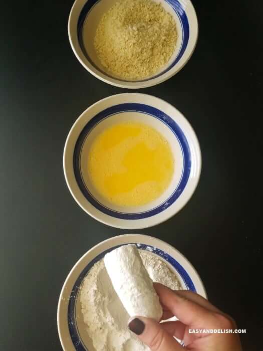 3 tigelas com os ingredientes da banana à milanesa -- farinha de rosca, farinha de trigo e ovos e uma banana sendo empanada