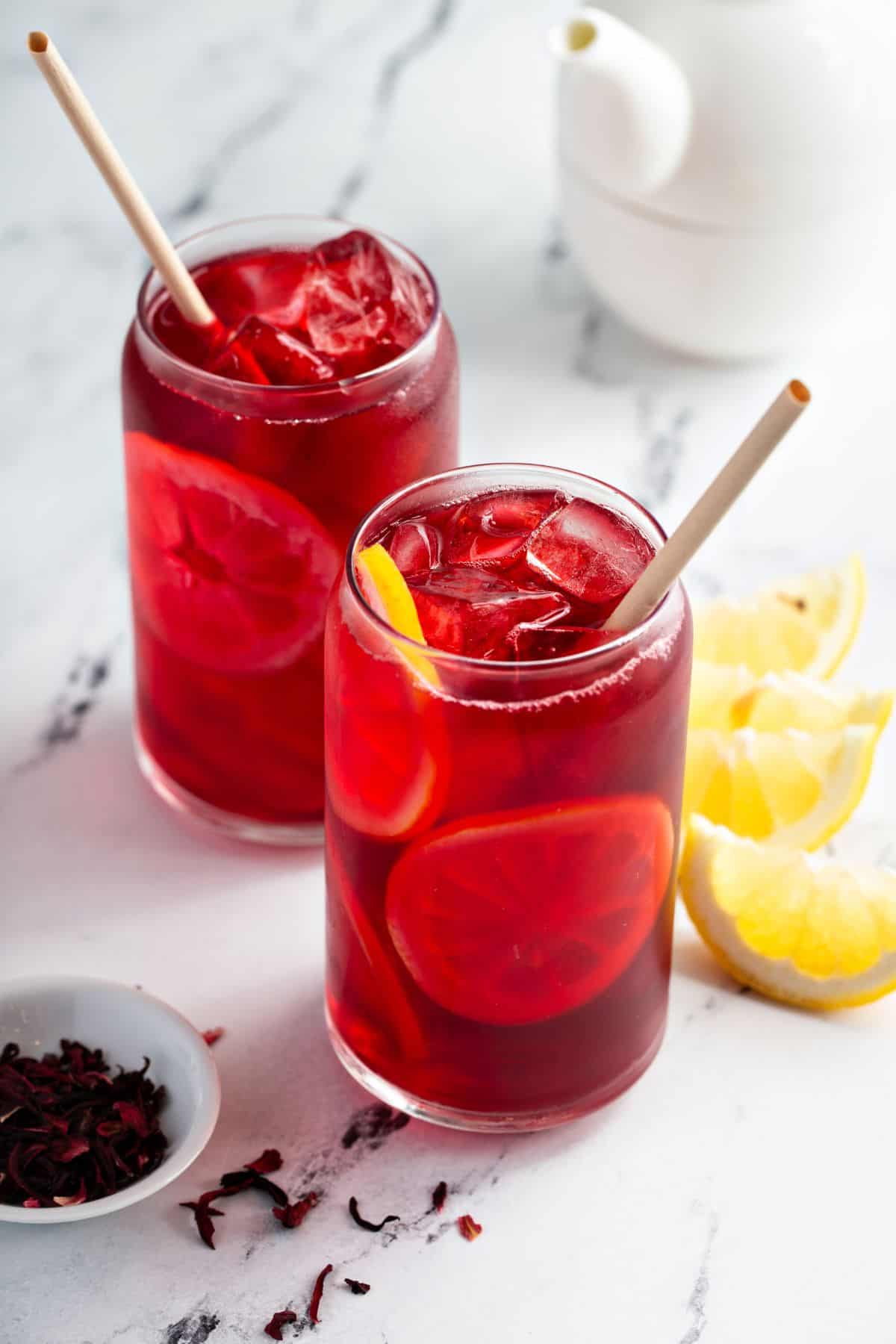 ICed hibiscus tea with lemon slices in glasses and dried hibiscus flowers on the side. 