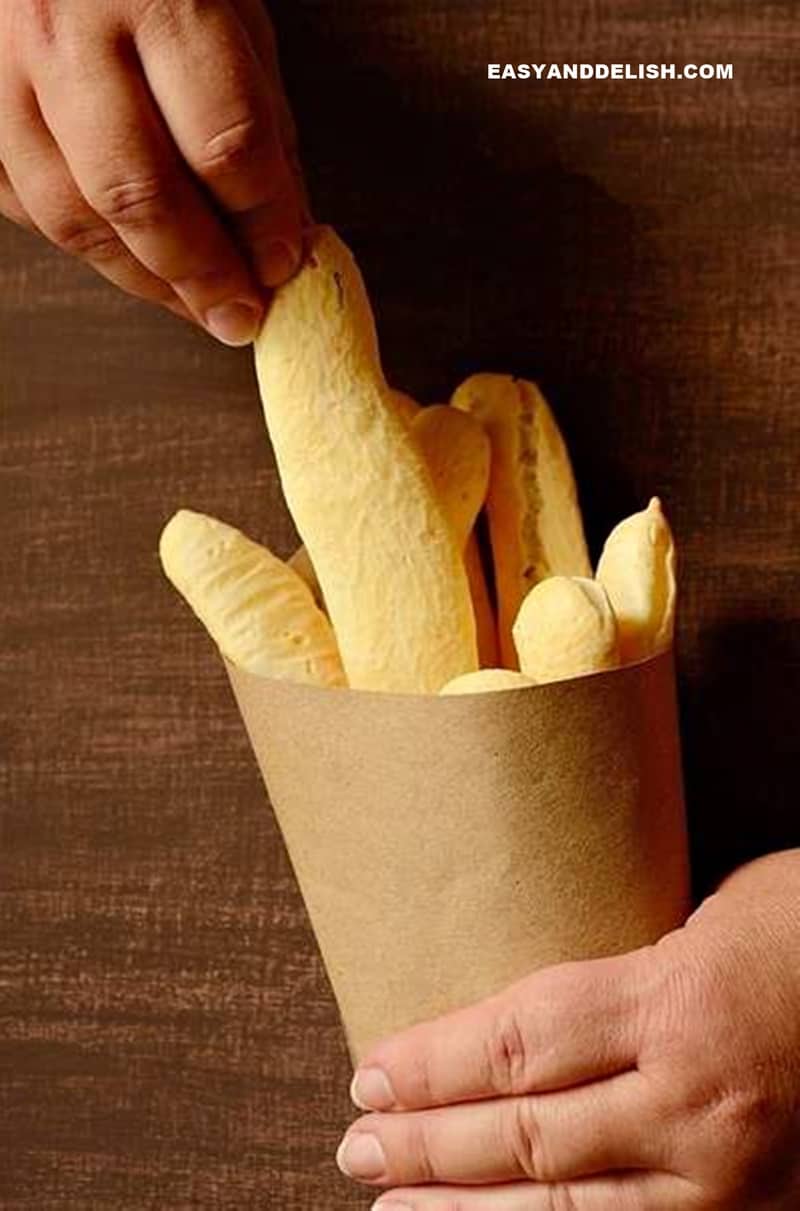 a hand picking a gluten-free breadstick in a paper bag