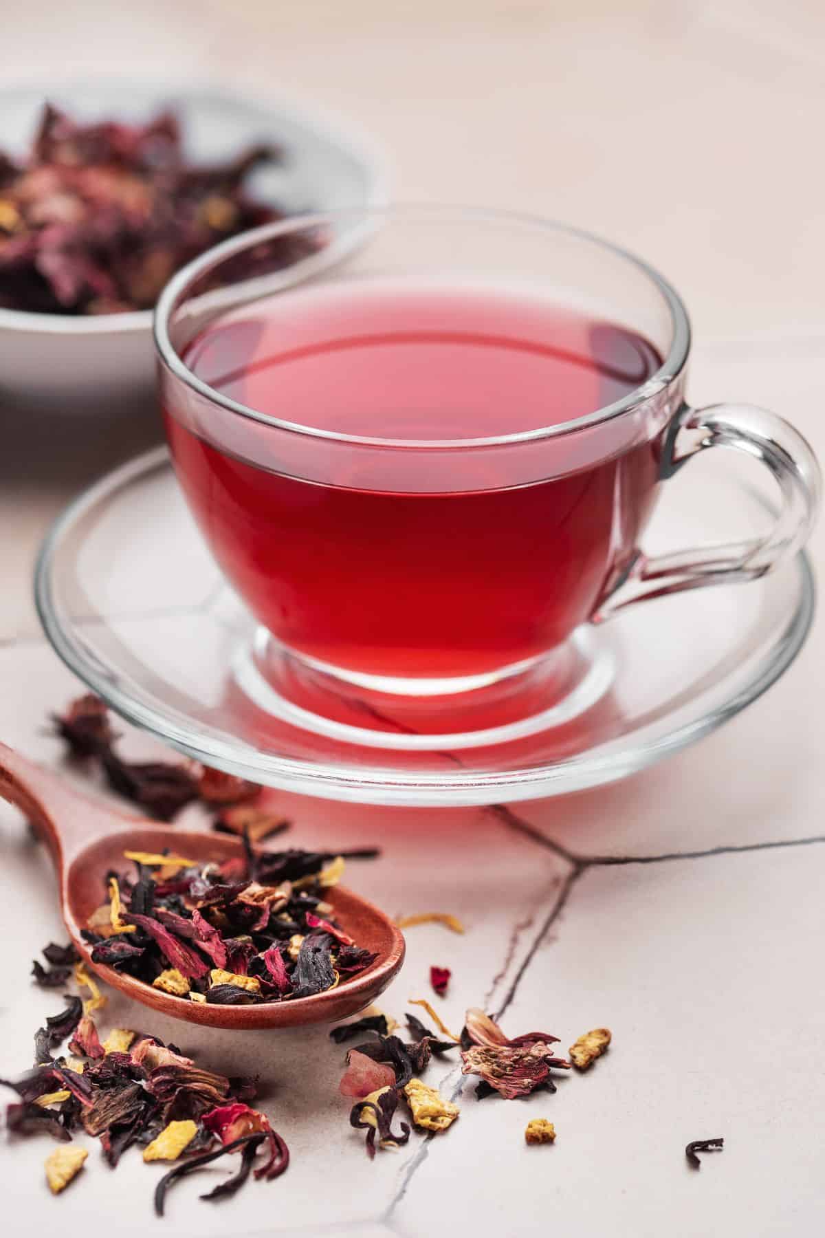 A cup of warm hibiscus tea with its dried flowers on the side. 