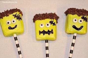 Three green frankenstein shaped marshmallow pops with candy eyes glued on