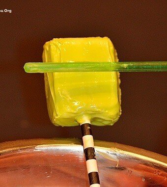 a green straw scrapes off excess candy melts from the frankenstein marshmallow square on a stick