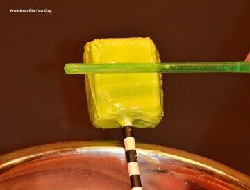 a green straw scrapes off excess candy melts from the frankenstein marshmallow square on a stick