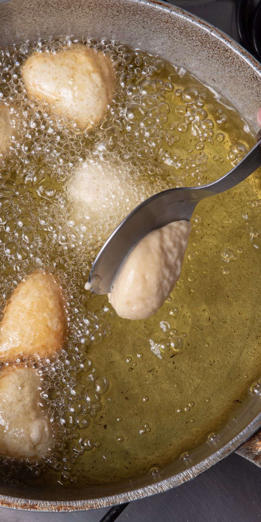 A spoon dropping dough into hot oil.