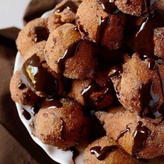 varios bolinhos de chuva empilhados numa bandeija com calda de chocolate
