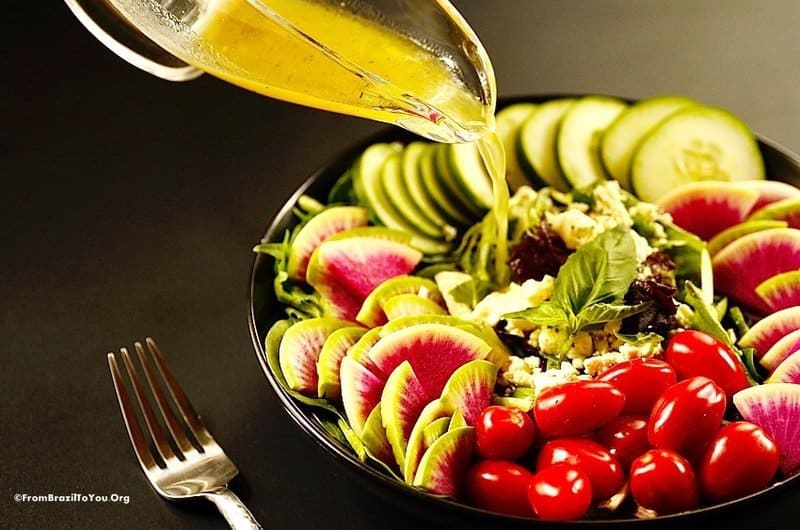 Vinaigrette dressing being poured over a raw salad of cucumbers, radishes, and tomatoes.