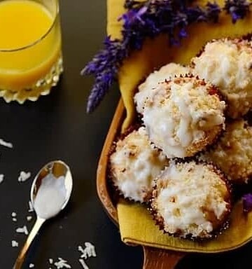 A pile of muffins on a board with a glass of orange juice