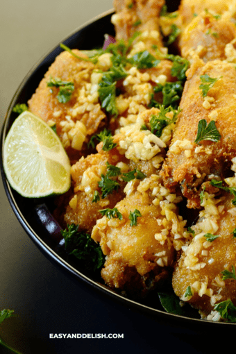 a close up of a plates full of fried chicken bites with lime wedges on the side