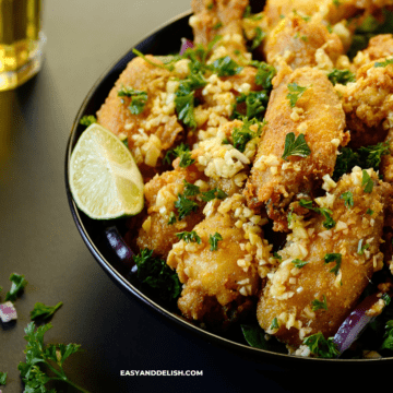 a close up of a plates full of fried chicken bites with lime wedges on the side