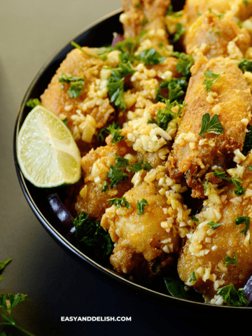 a close up of a plates full of fried chicken bites with lime wedges on the side