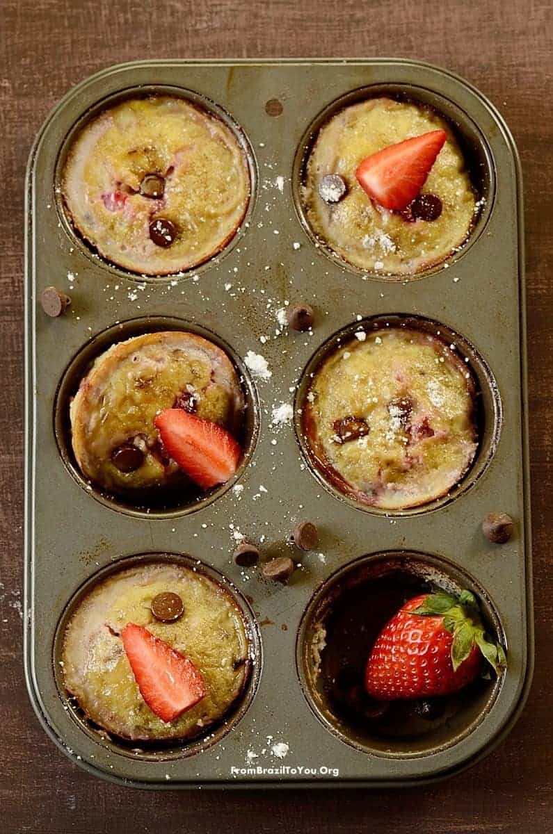 A muffin tin with baked muffins topped with strawberries