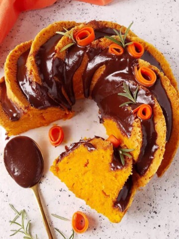 bolo de cenoura fofinho parcialmente fatiado com uma colher de cobertua de chocolate