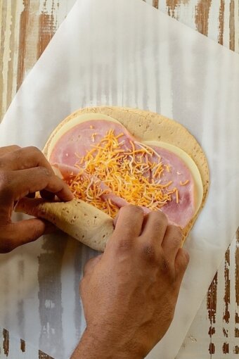 Ham and cheese flatbread being rolled up on a board